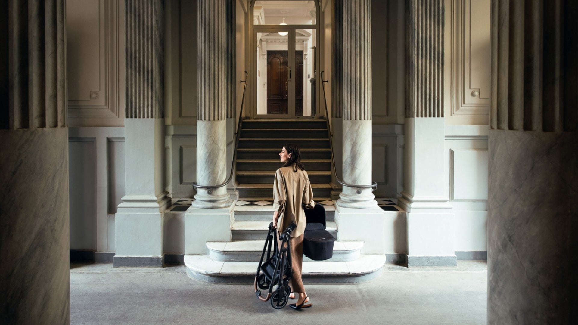 Women carrying folded Nuna SWIV stroller frame in one hand and Nuna SWIV bassinet in the other