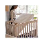 White Breathable Mini Crib Mattress - Parent Lowering into Natural Wood Mini Crib Wide Angle Nursery View | Bambi Baby