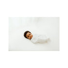 Baby lying on white surface in Swaddelini Kahlmi Massage Me swaddle with massage guide print - Overhead | Bambi Baby
